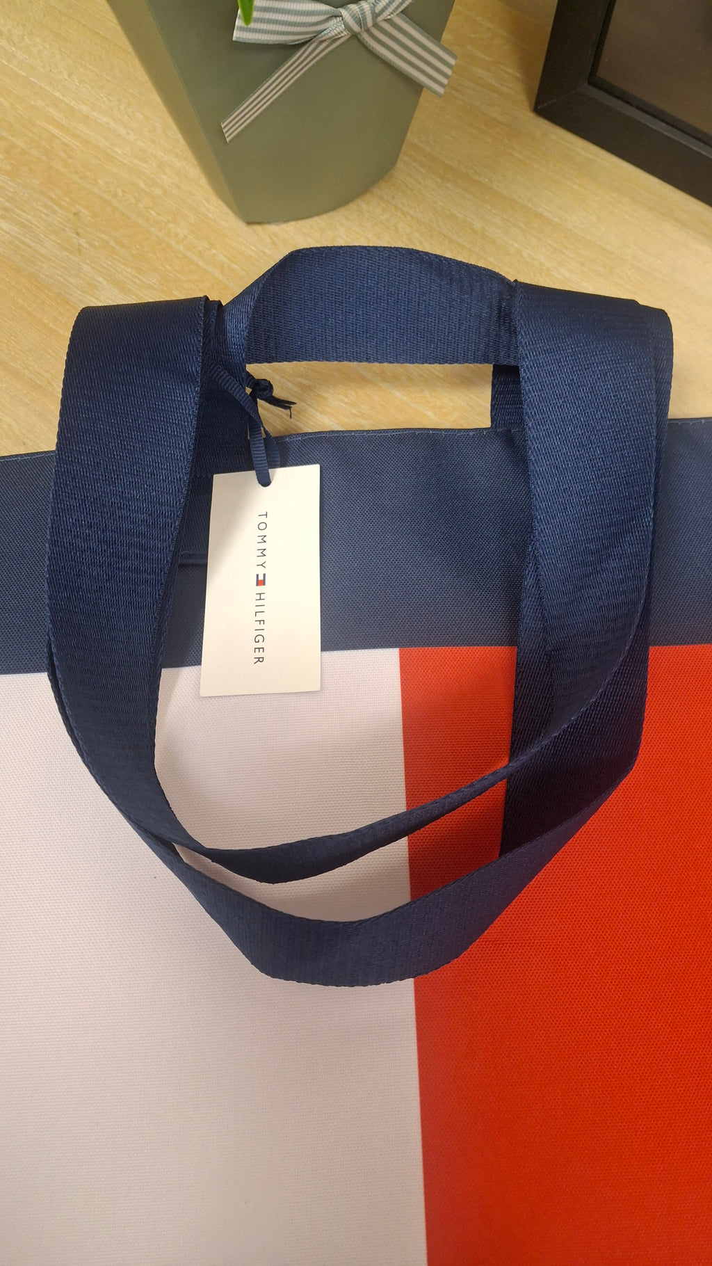 A navy blue fabric tote bag with a navy, white and red colour-blocked design, featuring a white hanging tag with the Tommy Hilfiger brand name.