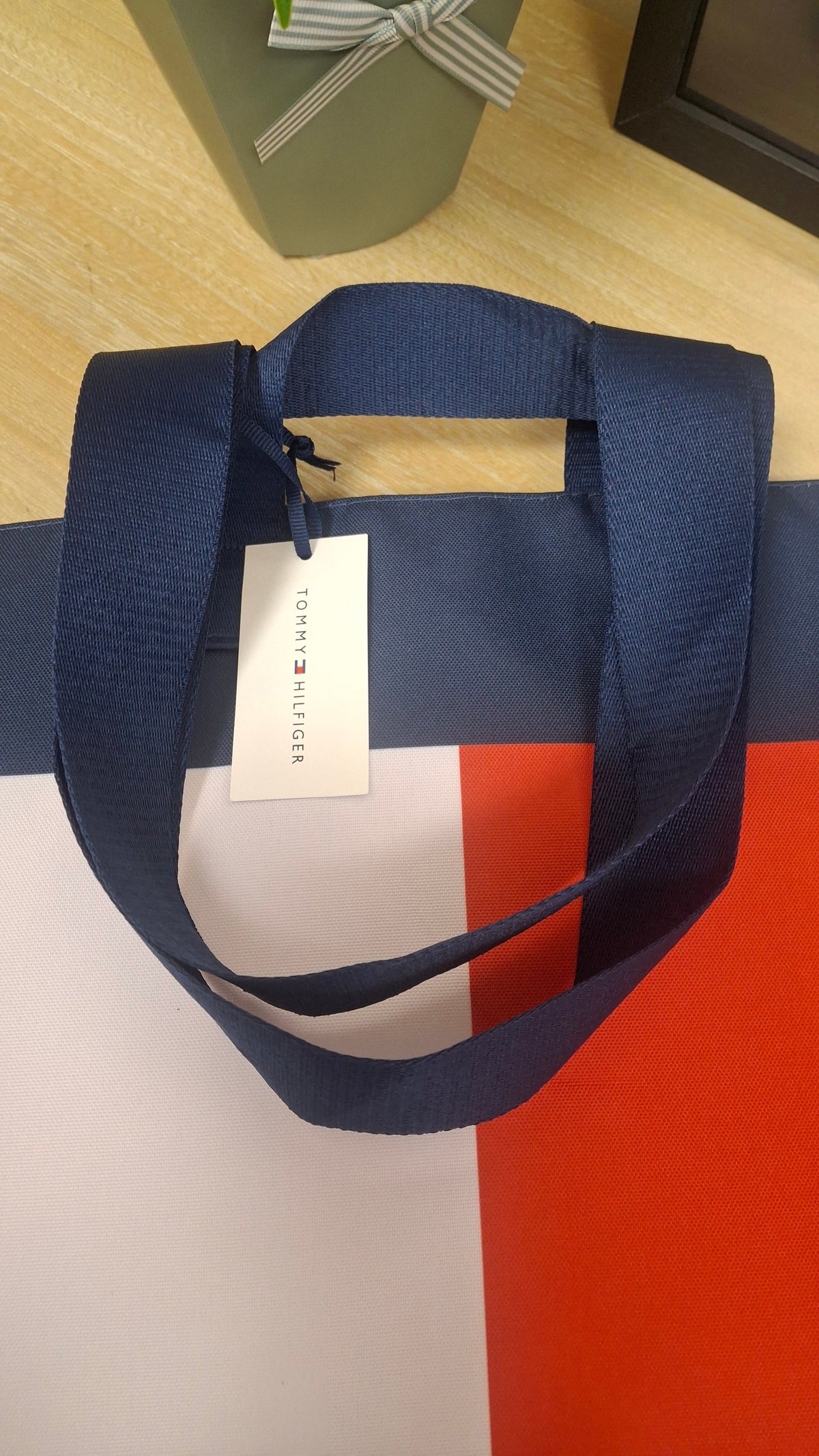 A navy blue fabric tote bag with a navy, white and red colour-blocked design, featuring a white hanging tag with the Tommy Hilfiger brand name.