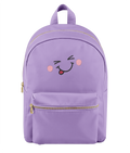 A pale lavender backpack with a front pocket featuring a cute embroidered winking face with pink cheeks and a red tongue. The backpack has gold-tone zippers and a top handle, shown against a plain white background.