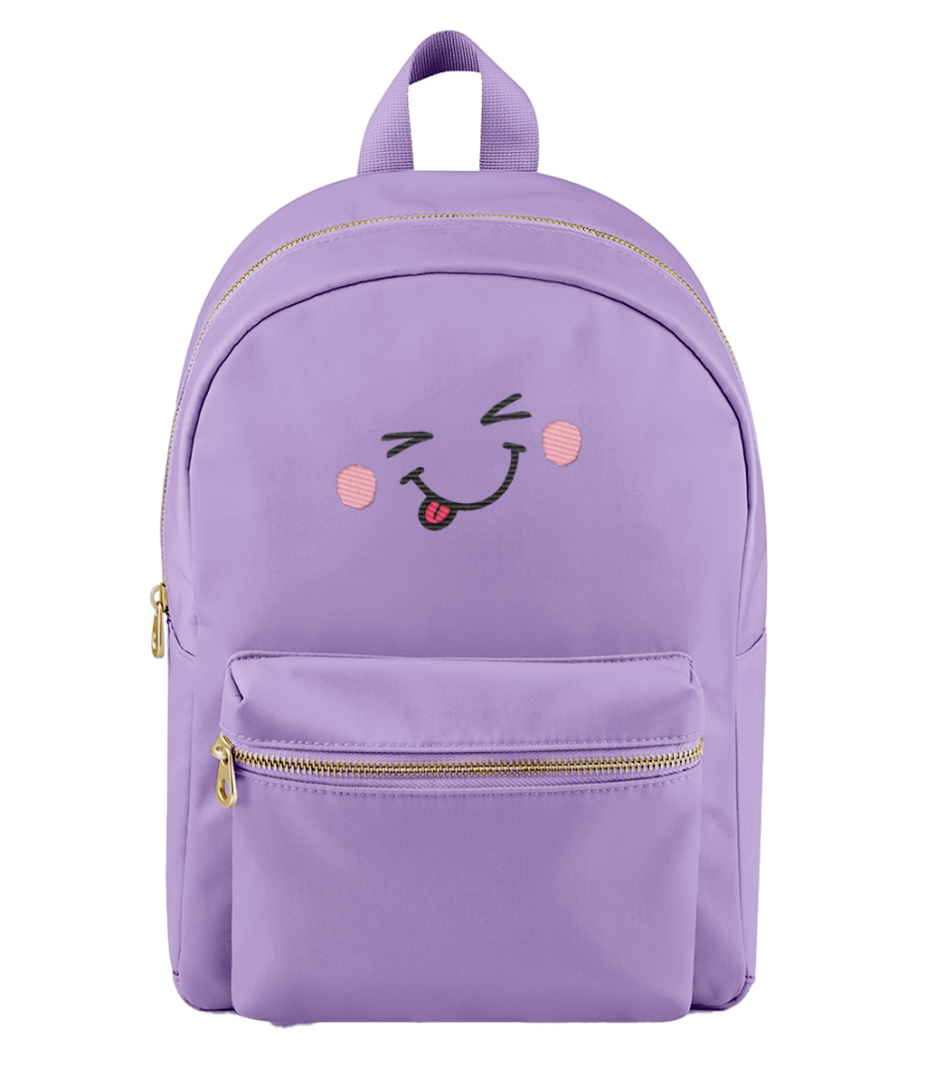 A pale lavender backpack with a front pocket featuring a cute embroidered winking face with pink cheeks and a red tongue. The backpack has gold-tone zippers and a top handle, shown against a plain white background.