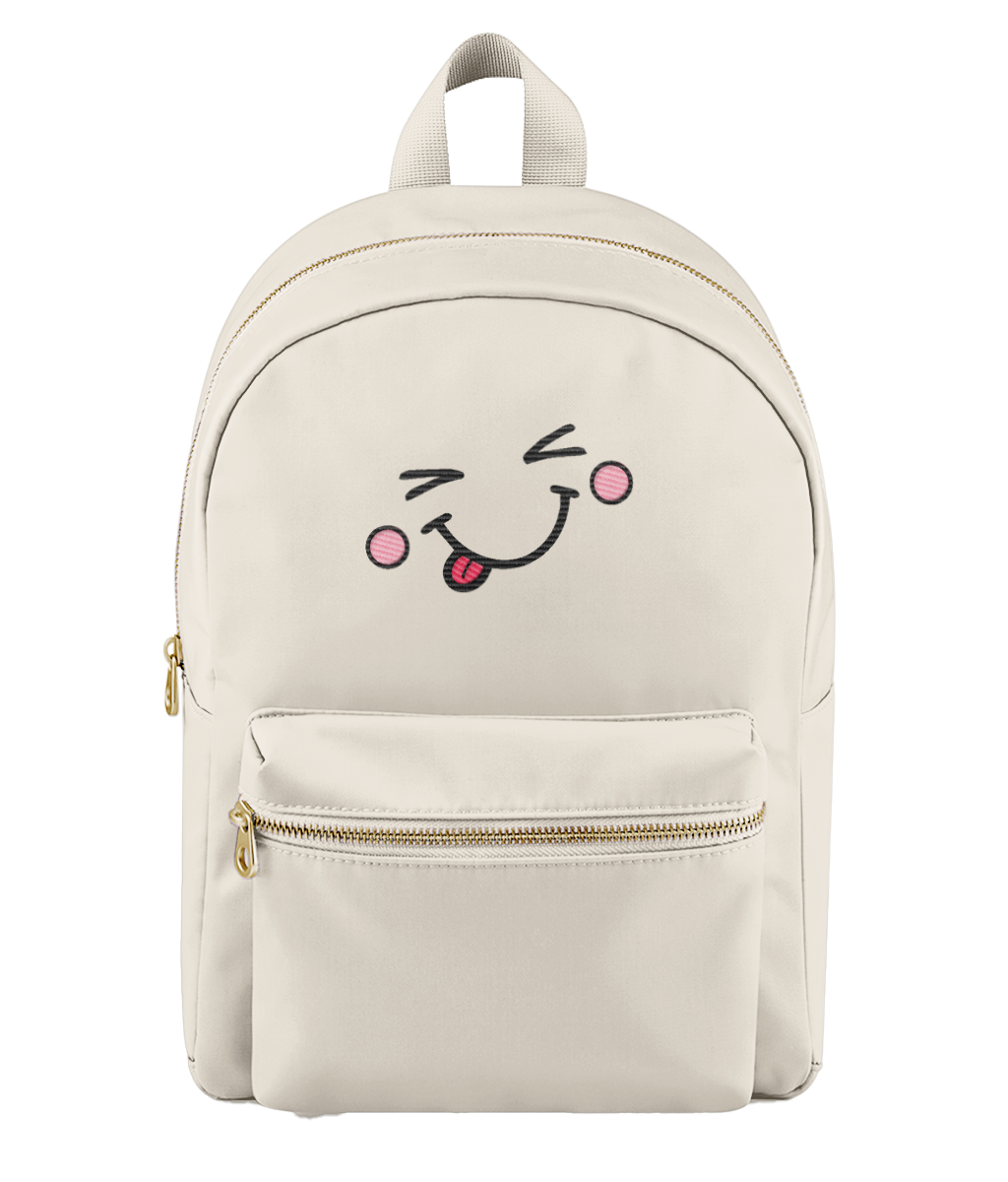 A cream-colored nylon backpack with a gold zipper and a cute embroidered face on the front pocket showing a winking eye, pink cheeks, and a sticking-out tongue.
