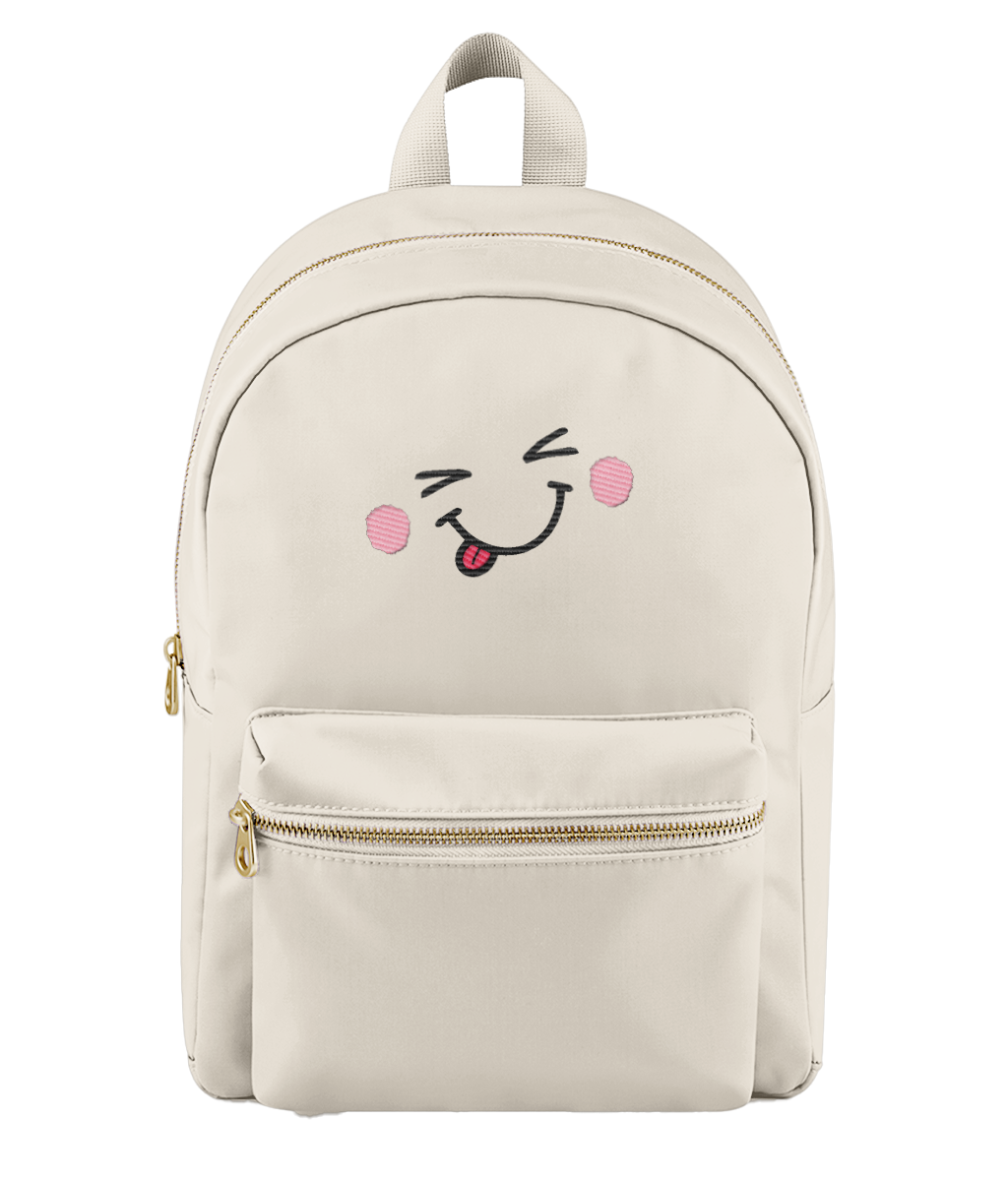 A cream-colored nylon backpack with a gold zipper and a cute embroidered face on the front pocket showing winking eyes, pink cheeks, and a sticking out tongue.