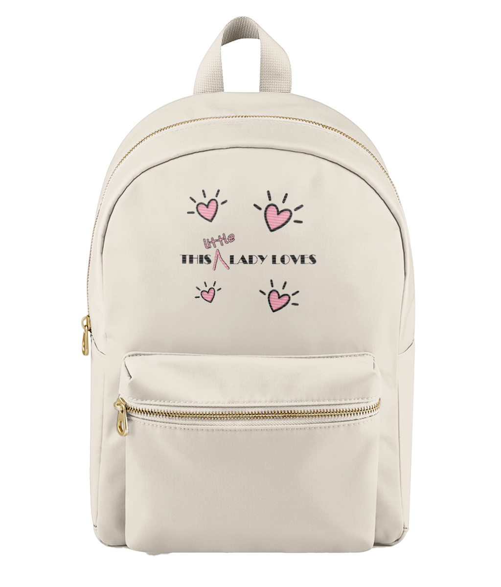 An off-white nylon backpack with gold zippers and a front pocket, featuring a pink and black graphic print that reads 'This Little Lady Loves' with heart illustrations.
