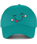 A teal green baseball cap featuring a playful embroidered face on the front with closed eyes, pink cheeks, and a pink tongue sticking out, shown against a plain white background.