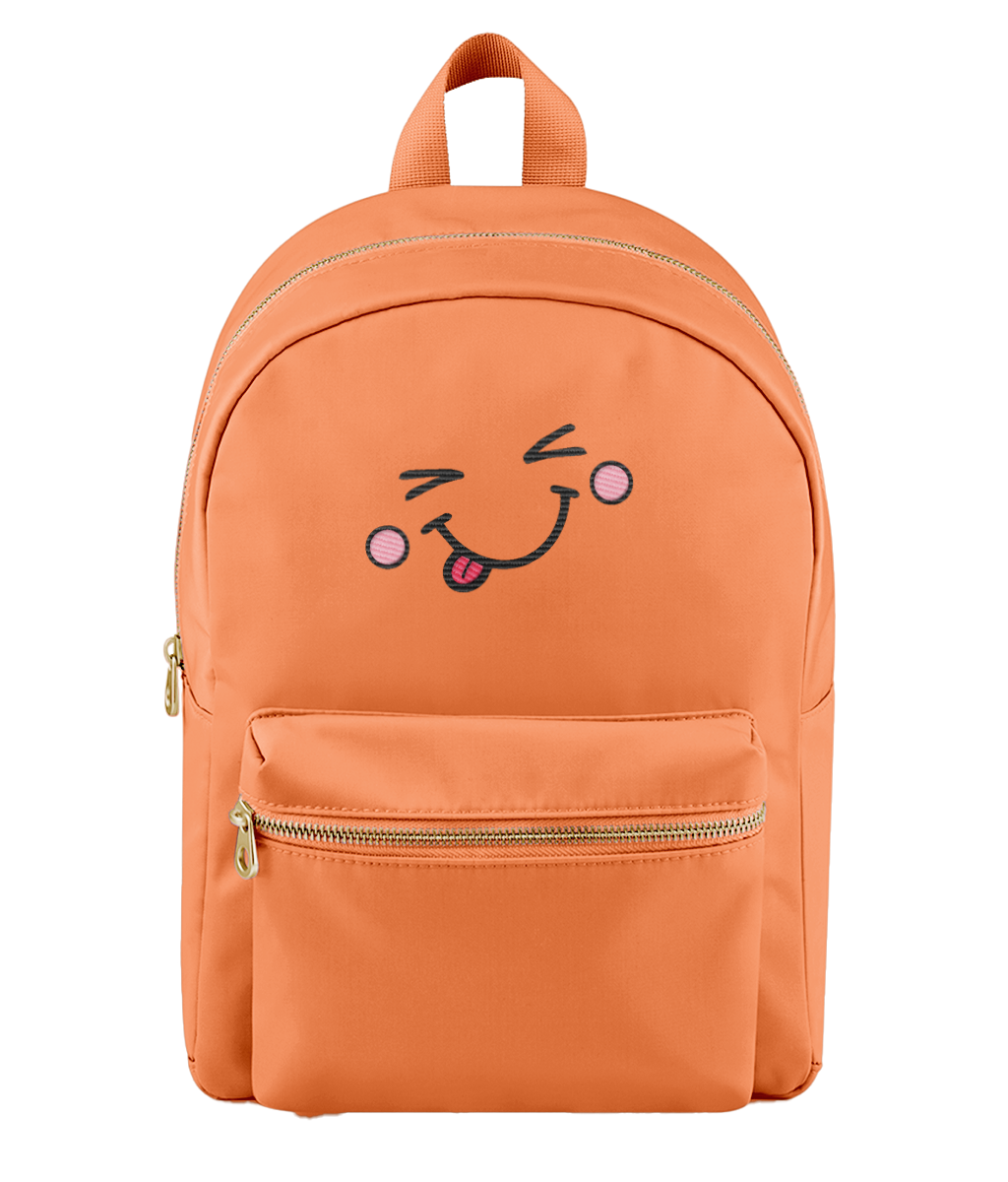 An orange nylon backpack with a cute embroidered face on the front pocket, featuring a winking eye, pink cheeks, and a sticking-out tongue. The backpack has a top handle, a main zippered compartment, and a front zippered pocket with gold-tone zippers.