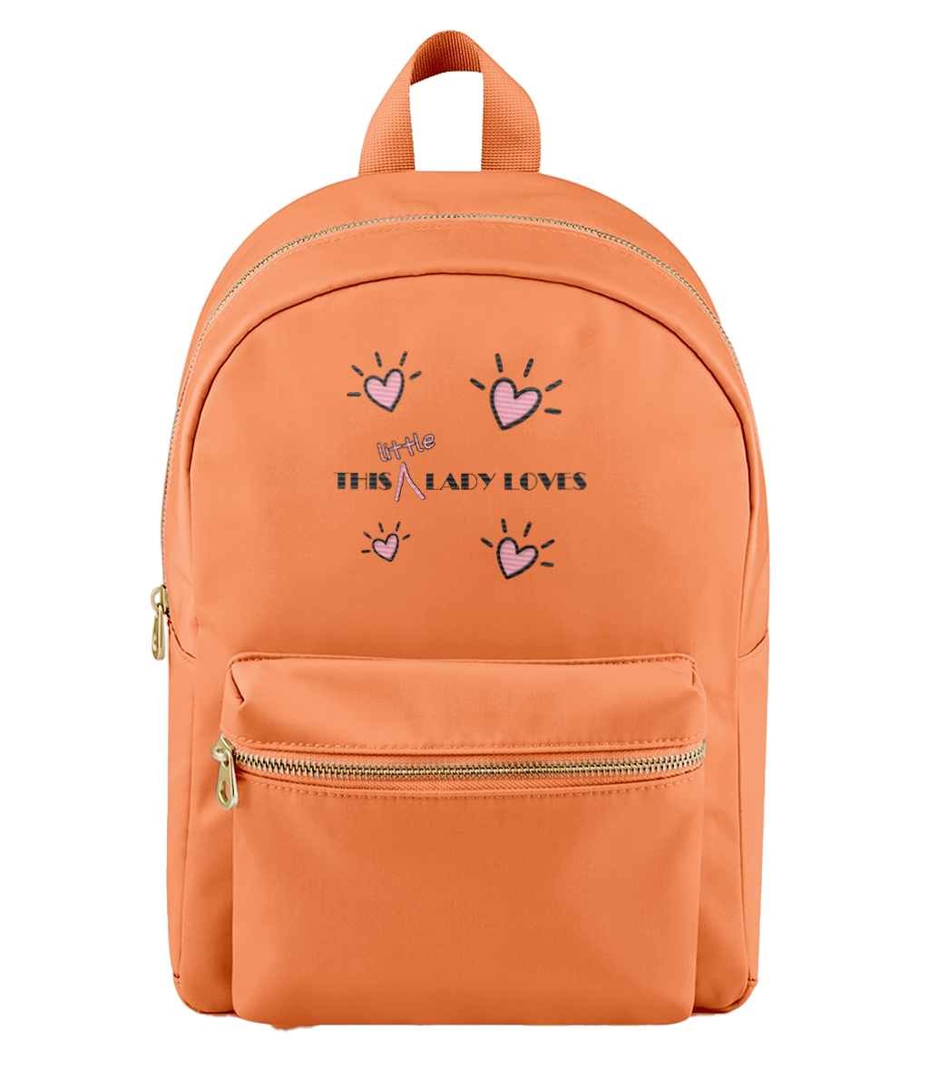 An orange backpack with a front zippered pocket and top handle, featuring a graphic print of pink hearts and the text 'this little lady loves' in black and pink on the front.