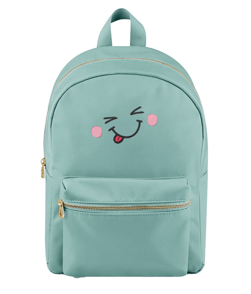 A mint green backpack with a gold zipper and a cute embroidered face on the front pocket featuring pink cheeks and a sticking-out tongue.