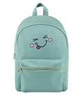 A mint green backpack with a gold zipper and a cute embroidered face on the front pocket showing winking eyes, pink cheeks, and a sticking out tongue.