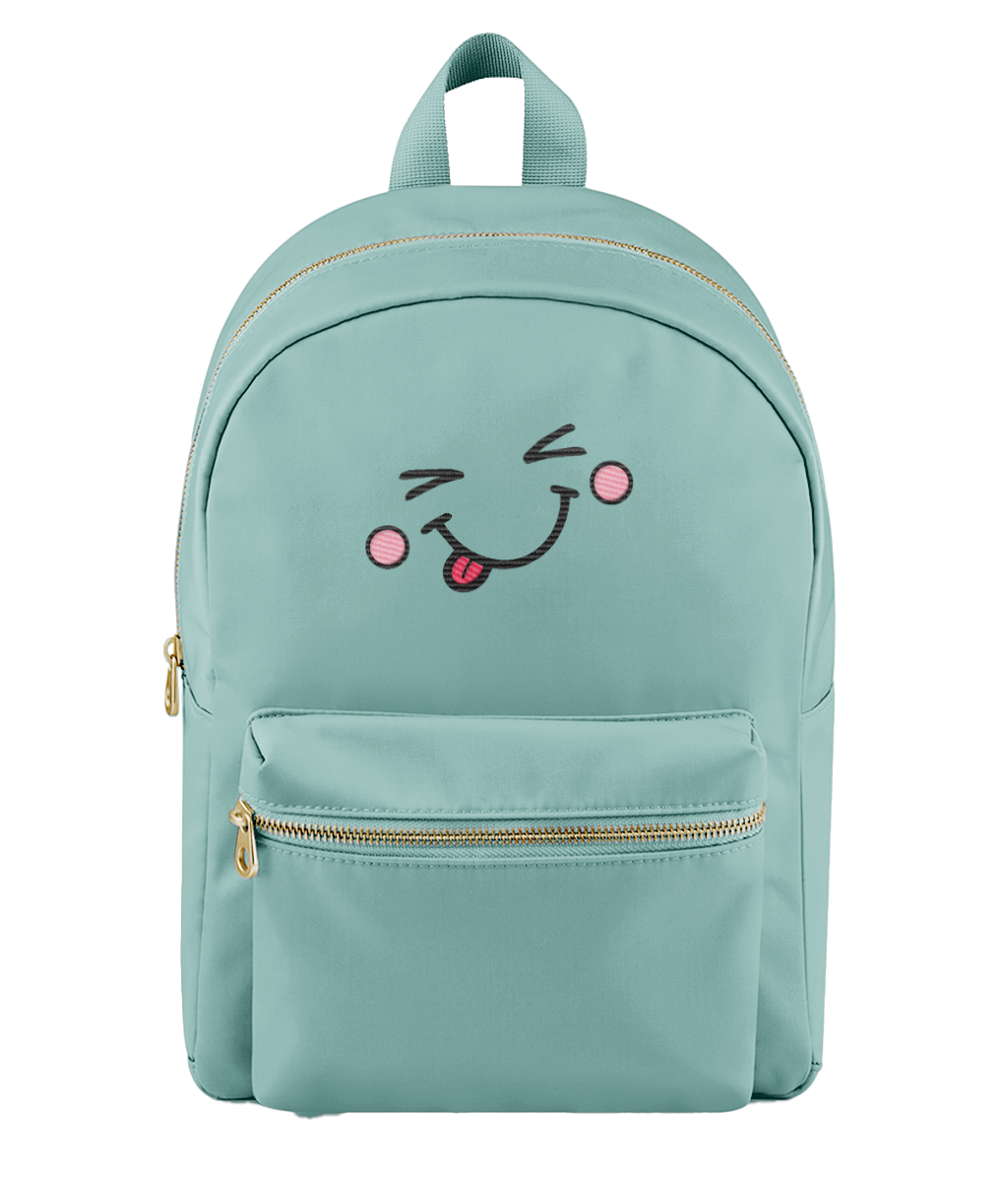 A mint green backpack with a gold zipper and a cute embroidered face on the front pocket showing winking eyes, pink cheeks, and a sticking out tongue.